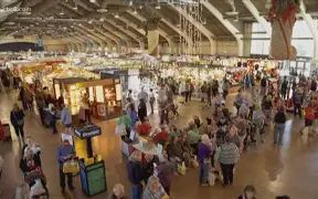 Busy indoor market scene with numerous stalls, shoppers, and vendors in a large hall.