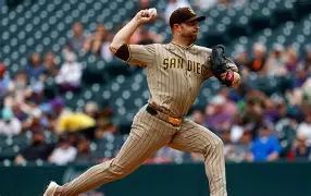 Baseball pitcher in Padres uniform mid-pitch on the mound with blurred stadium seating in the background.