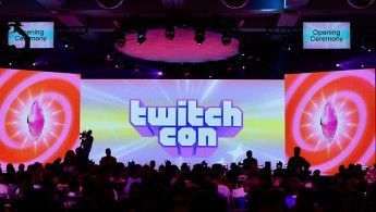 Crowd gathered in front of a brightly lit stage at TwitchCon opening ceremony with a central screen displaying the TwitchCon logo.