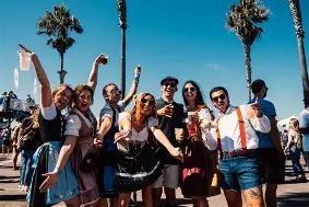 Group of friends posing and cheering at a sunny outdoor event with palm trees in the background.